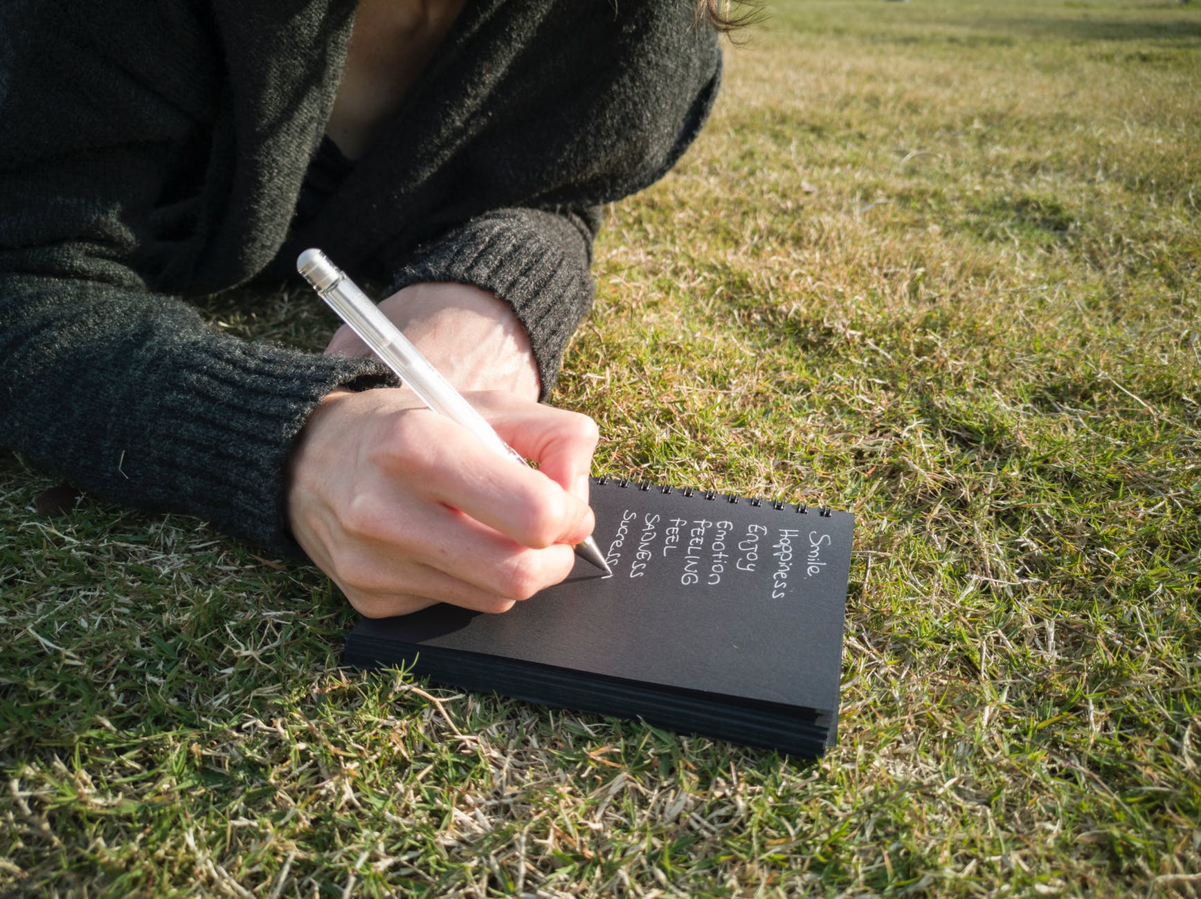 person writing on book lying down on the ground